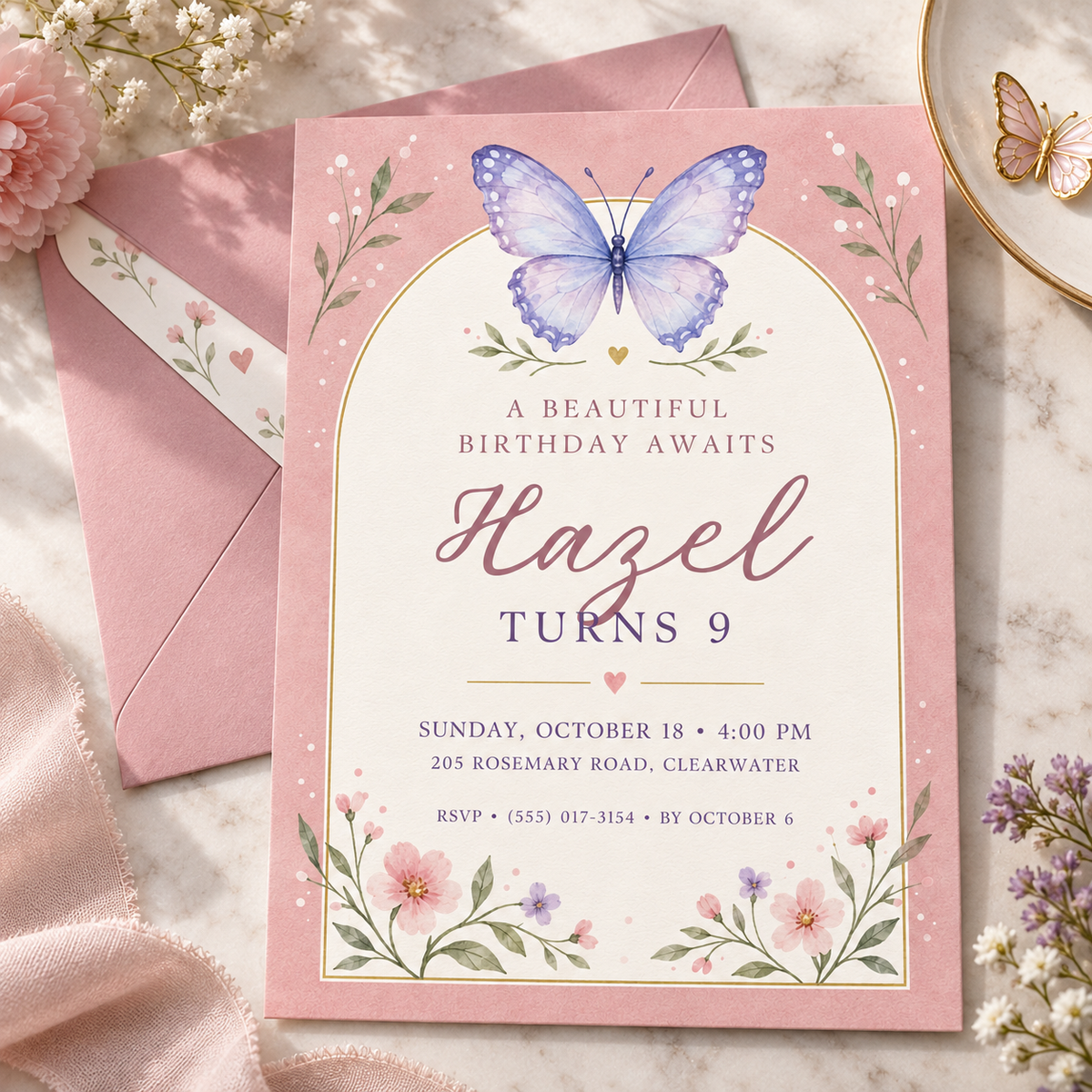 Butterfly arch invitation beside a pink envelope and fresh flowers