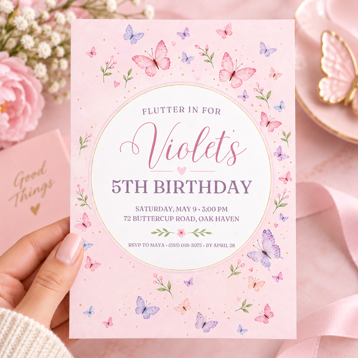 Hand holding a blush pink butterfly birthday invitation with a white gold-rimmed circle