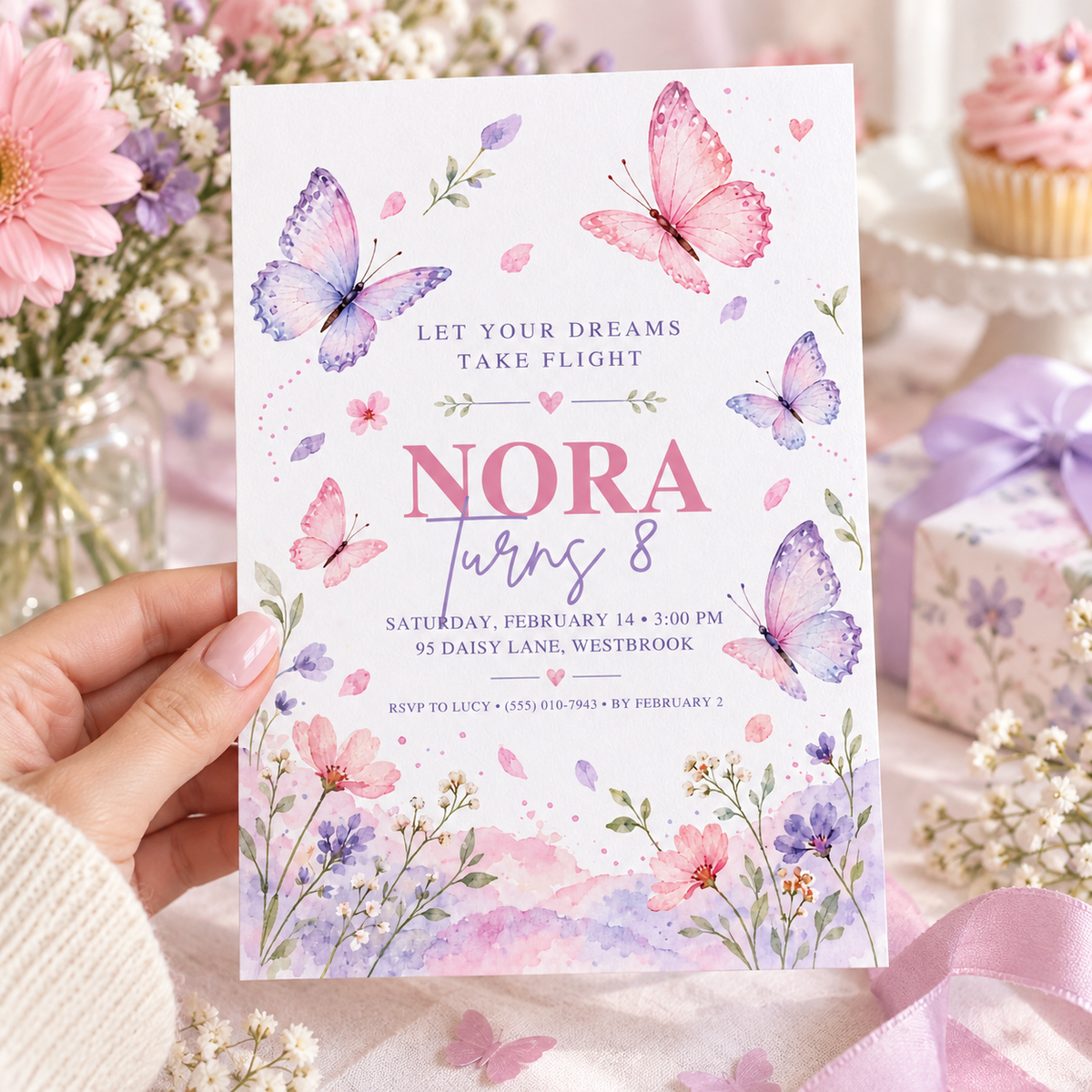 Hand holding a let your dreams take flight butterfly invitation with a wildflower meadow