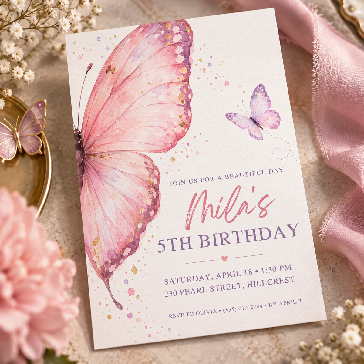 Pink butterfly invitation angled on cream fabric beside a gold butterfly dish