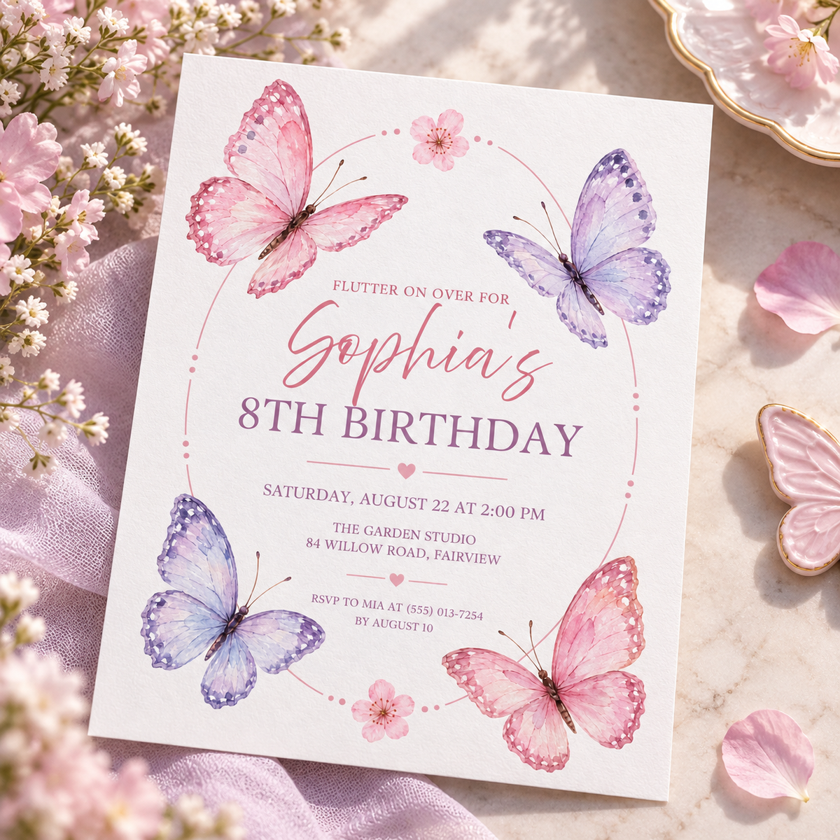 Pink butterfly invitation angled on pink linen with paper butterflies